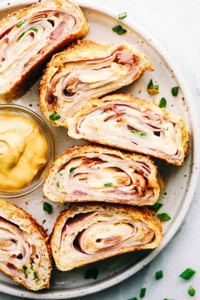 Easy Ham and Swiss Stromboliย can be anything you want it to be! Breakfast? Yes. Brunch? You bet. Dinner? Of course! This meal is a triple threat. It's easy enough to be a side dish. But so good it will be the star of the table.ย Ham and Swiss Stromboli on a white plate.
