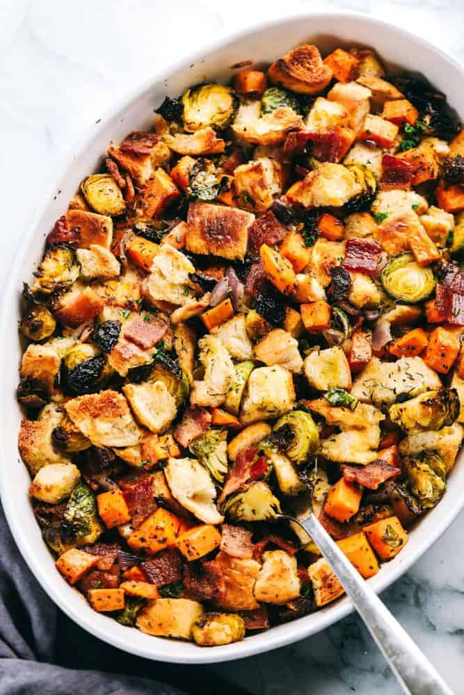 Roasted Autumn Vegetable Stuffing is the perfect side dish for your holiday meal. Filled with roasted autumn vegetables and bacon, this is the perfect addition to the dinner table. Roasted autumn vegetable stuffing on in a white baking dish with a silver spoon pulling up part of the stuffing.