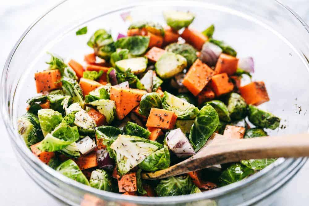 Roasted Autumn Vegetable Stuffing is the perfect side dish for your holiday meal. Filled with roasted autumn vegetables and bacon, this is the perfect addition to the dinner table. Chopped up carrots, brussels sprouts and red onions being stirred together with seasoning from McCormick using a wooden spoon and a glass bowl.