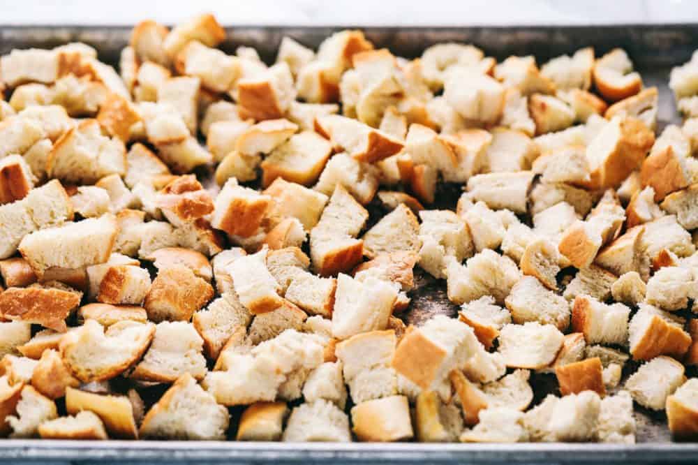 Roasted Autumn Vegetable Stuffing is the perfect side dish for your holiday meal. Filled with roasted autumn vegetables and bacon, this is the perfect addition to the dinner table. Chunks of bread on a baking sheet getting ready to be roasted to use in the Roasted autumn vegetable stuffing.