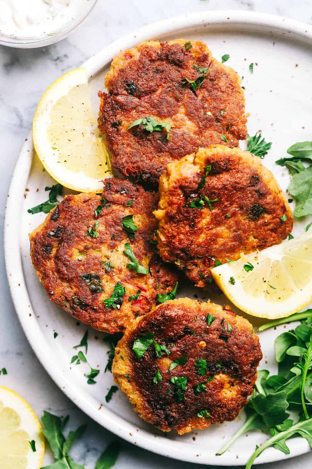 Salmon Croquettes are pan fried and packed with so many great flavors. These make a quick and easy weeknight meal and areย delicious with aย tartarย sauce!ย Salmon Croquettes on a white plate with freshly slices lemons.