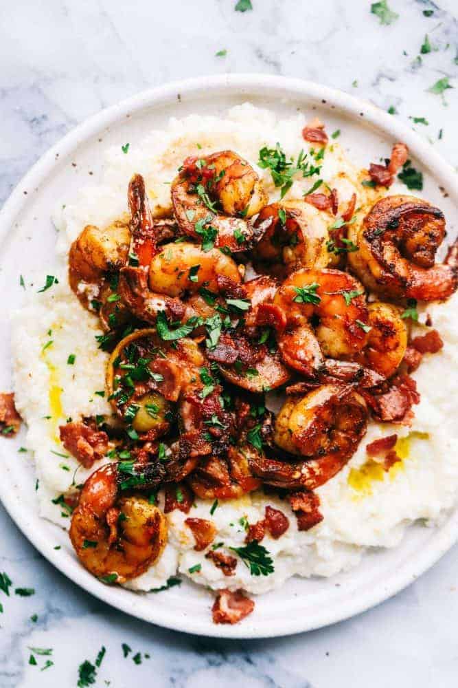 Cajun Garlic Shrimp and Grits are the PERFECT savory dish that you will want on your table. Best part is, it's easy and will make any busy week night delicious. Cajun garlic shrimp and grits on a white plate.