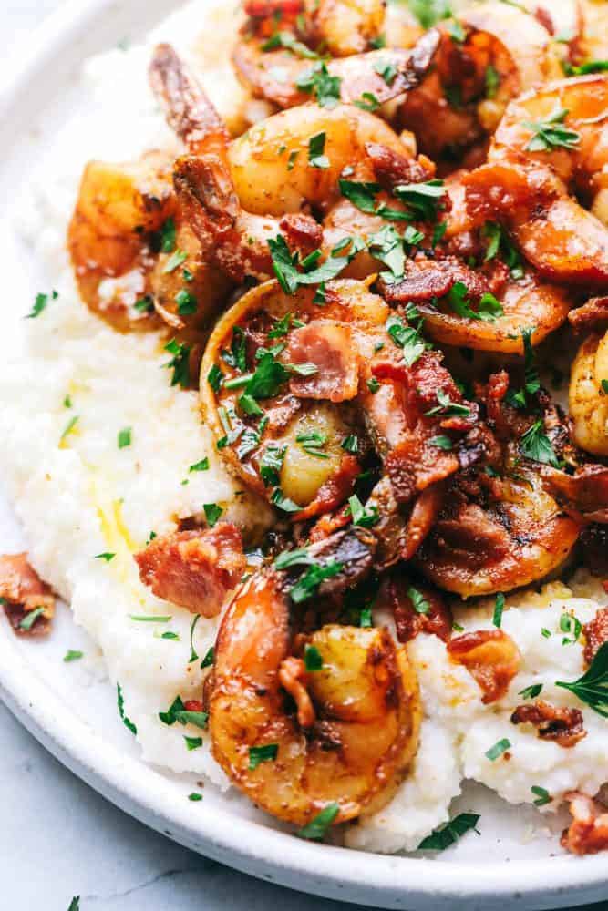 Cajun Garlic Shrimp and Grits are the PERFECT savory dish that you will want on your table. Best part is, it's easy and will make any busy week night delicious. Garlic shrimp and grits on a white plate.