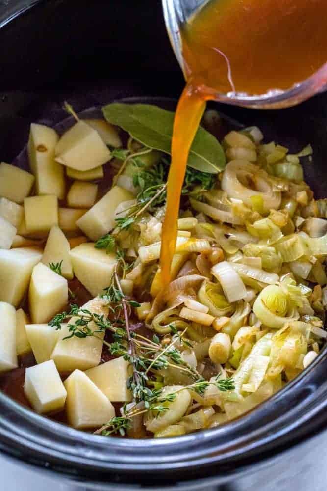 Slow Cooker Potato Leek Soup serves up a satisfying bowl of creamy pureed vegetables. The caramelized onions and leeks bump up the flavor as it gently simmers with the flaky potatoes and herbs. You wonโt believe how easy it is to create a restaurant quality dish in the crock-pot! Broth being poured over leeks and potatoes inside a slow cooker.