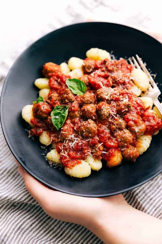 Sausage Tomato Gnocchi is a flavorful tomato sauce with miniature sausage "meatballs" served over gnocchi. A quick and easy meal that the family will all go crazy for!ย Sausage tomato gnocchi in a black bowl with a fork on the side.