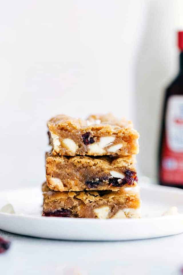 White Chocolate Cranberry Blondies are loaded with white chocolate chips, and dried cranberries. These are soft, chewy, and perfect for the holidays. Three white chocolate cranberry Blondies stacked on top of each other to show the chunks of white chocolate cranberry in the middle.