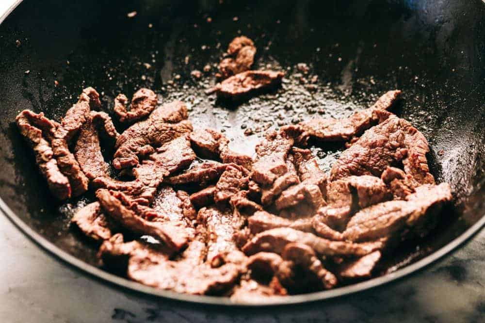 Garlic Beef and Broccoli Noodles is made with tender melt in your mouth beef in the most amazing garlic sauce. Add some mushrooms, broccoli and noodles for an amazing meal in one! Garlic beef being cooked in a skillet.
