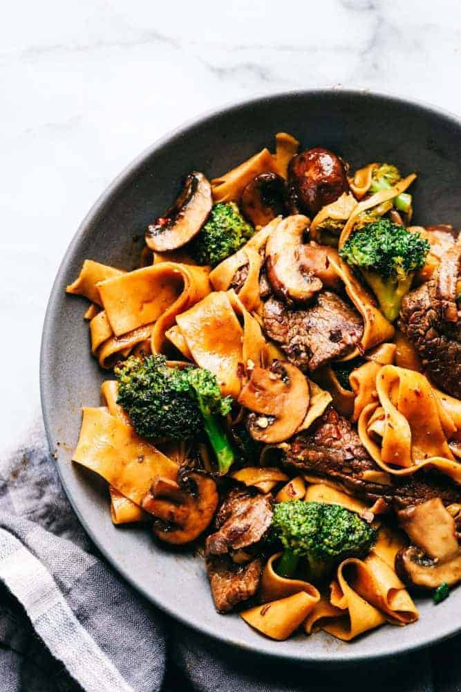 Garlic Beef and Broccoli Noodles is made with tender melt in your mouth beef in the most amazing garlic sauce. Add some mushrooms, broccoli and noodles for an amazing meal in one! Garlic beef and broccoli noodles and a gray bowl.