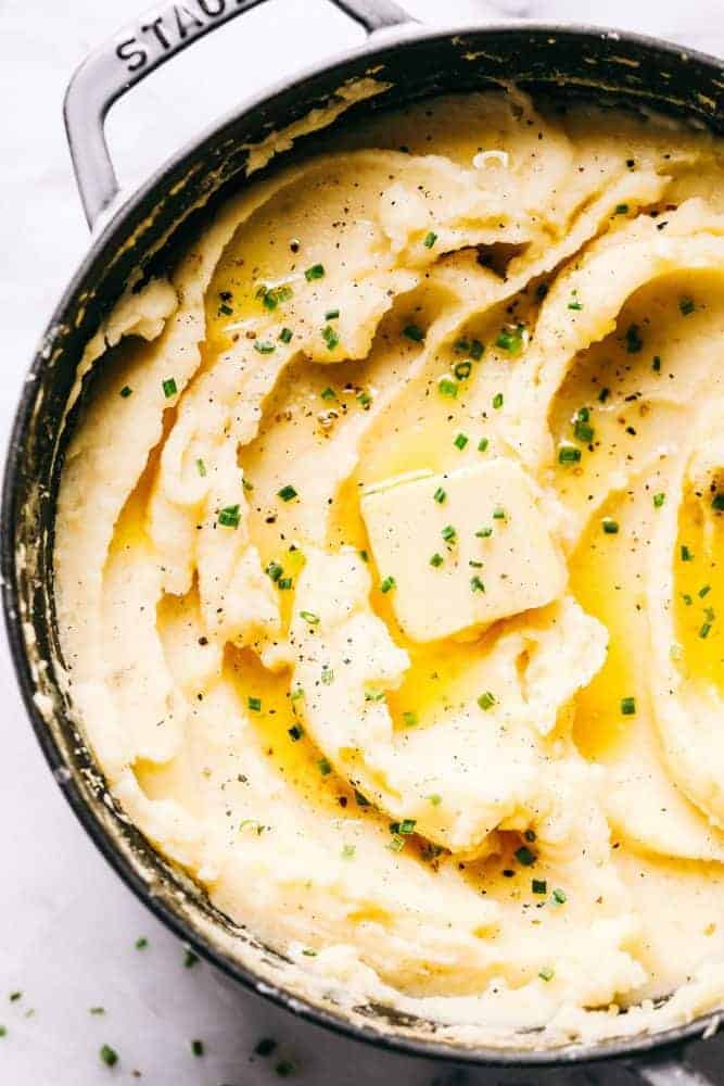 Dad's Famous Mashed Potatoes are always the star of a dinner table! Perfectly creamy, buttery, and they have such amazing flavor. People are always begging him to make the recipe! Mashed potatoes in a Staub sauce pan with a slice of butter melted on top of the mashed potatoes with chives garnished on top.