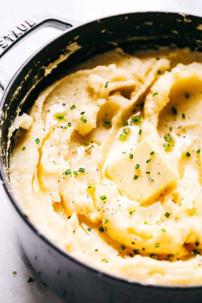 Dad's Famous Mashed Potatoes are always the star of a dinner table! Perfectly creamy, buttery, and they have such amazing flavor. People are always begging him to make the recipe! Dad's Famous Mashed Potatoes in a Staub sauce pan with a slice a butter over top.