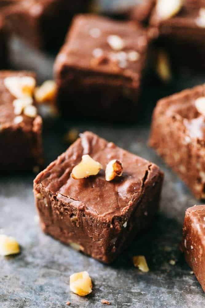 Fantasy Fudge is the creamiest, dreamiest most delicious classic fudge recipe. The fudge just melts in your mouth and is so easy to make with no thermometer required! Fantasy fudge cut into 1 inch pieces garnished with walnuts over top sitting on a black countertop