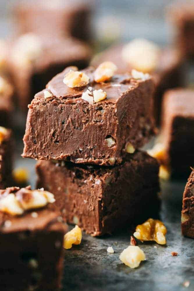 Fantasy Fudge is the creamiest, dreamiest most delicious classic fudge recipe. The fudge just melts in your mouth and is so easy to make with no thermometer required! Fantasy fudgeStacked on top of each other with walnuts garnished over top and on the black countertop.