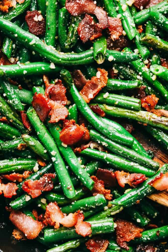 Garlic Parmesan Green Beans with Bacon is such a delicious and classic side dish. Tender green beans cooked in garlic and parmesan with added bacon will be a winner at the dinner table! An up close photo of the garlic Parmesan green beans with the chopped up cooked bacon and garnished with Parmesan sprinkles.