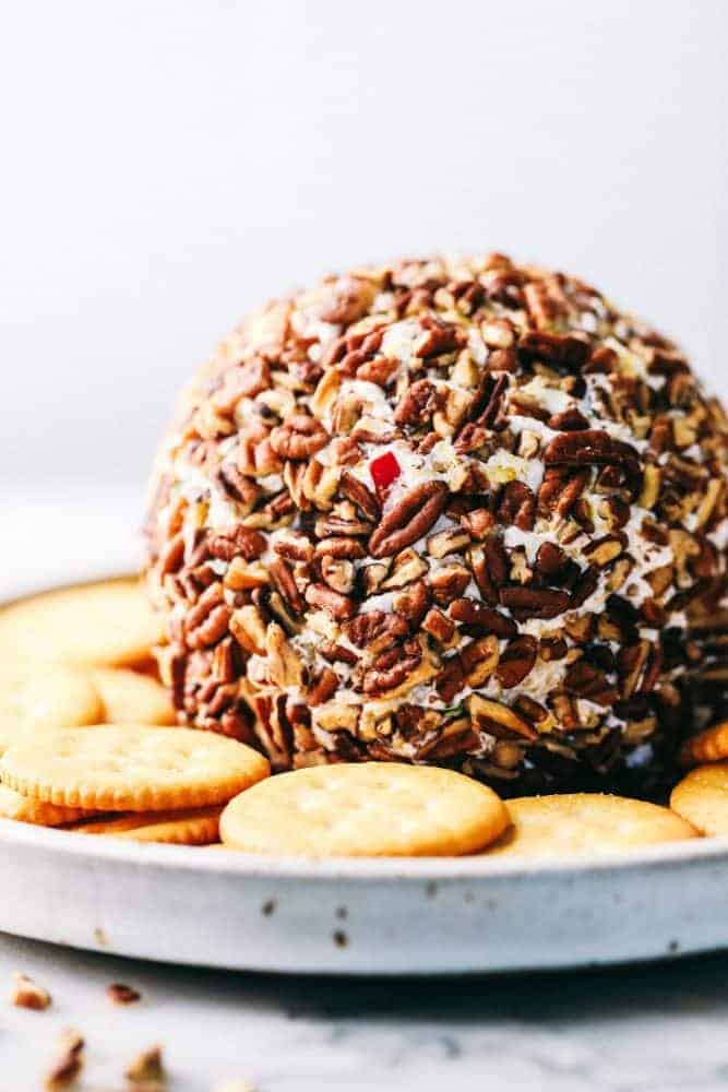 Pineapple Cheese Ball is the next best twist on a favorite classic. With Different textures and flavors it will be the hit at your next gathering! A pineapple cheese ballWith Ritz crackers are around it and white plate.