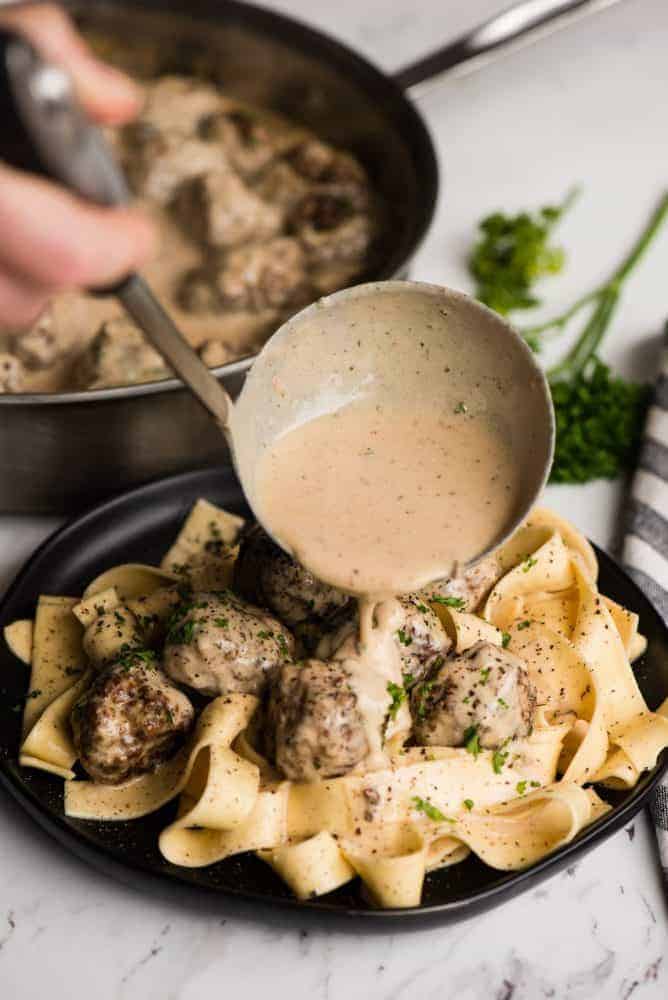 Swedish Meatball Pasta combines flavorful homemade pork and beef Swedish meatballs with a heavenly cream sauce and perfectly cooked pasta. Swedish meatball pasta having this creamy sauce poured over top from the ladle.