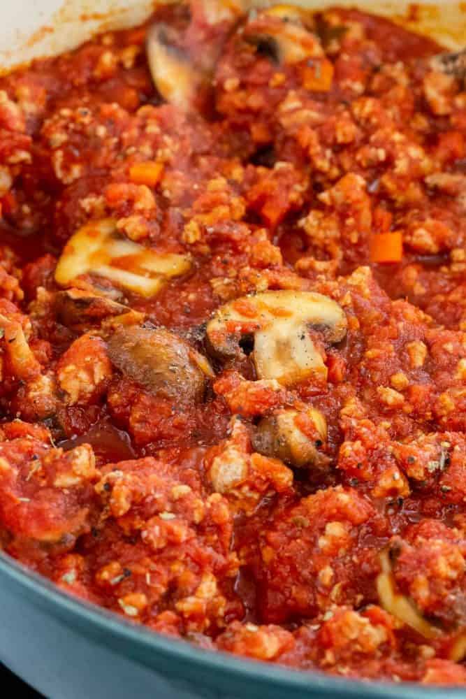 Turkey Bolognese with Roasted Spaghetti Squash is a hearty Italian feast with a low carb twist. Ground turkey is gently simmered with carrots, onions, and mushrooms in a rich tomato sauce. The flesh of the squash separates into strands to mimic pasta noodles for a tasty vegetable-packed meal. close up photo of meat sauce in a pan
