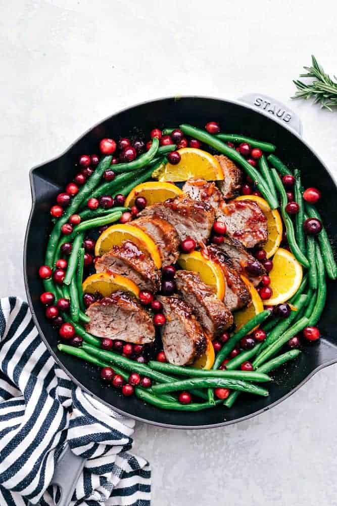 Roasted Cranberry Orange Pork Tenderloin with Green Beans is such a flavorful and easy meal. The cranberry orange glaze is perfect on top of the pork and green beans. This will be the star of your holiday dinner table! Roasted cranberry orange pork tenderloin with green beans and a black Staub skillet.