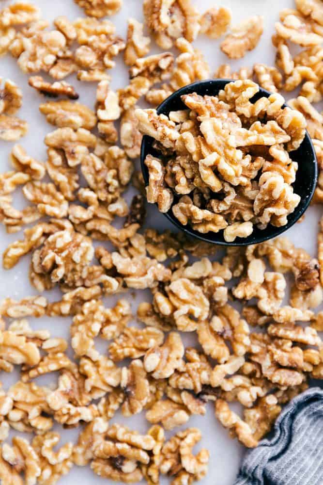 Snow Kiss Cookies are buttery cookies with walnuts that just melt in your mouth. They get dusted in powdered sugar and are are such an amazing classic cookie! Walnut halves spread out on the table. There are some in a bowl as well.