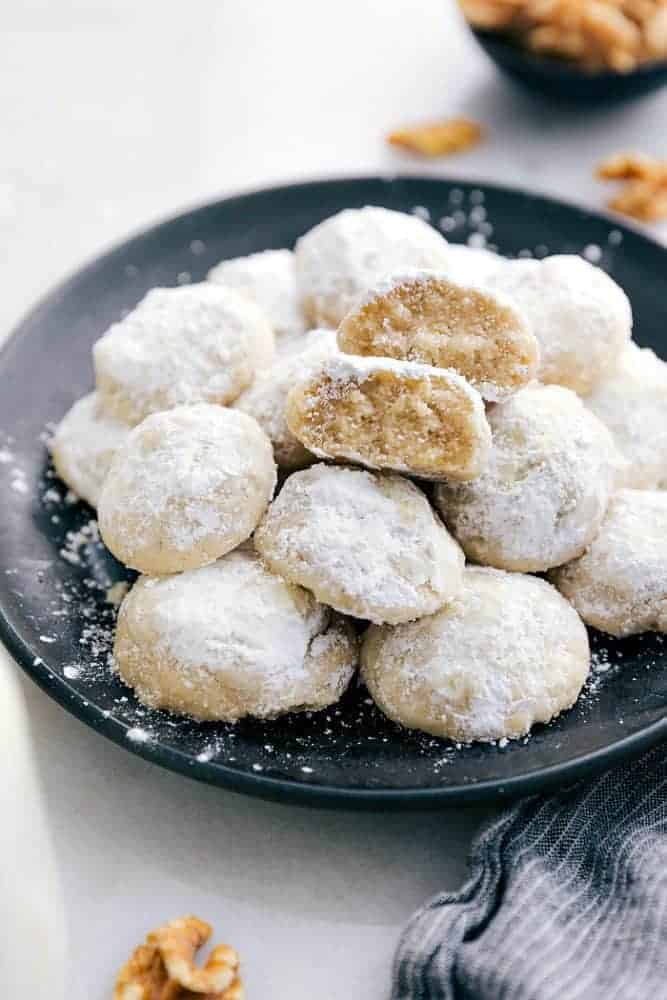 Snow Kiss Cookies are buttery cookies with walnuts that just melt in your mouth. They get dusted in powdered sugar and are are such an amazing classic cookie! Snow kiss cookies on a black plate.