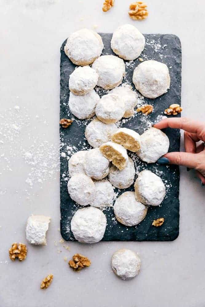 Snow Kiss Cookies are buttery cookies with walnuts that just melt in your mouth. They get dusted in powdered sugar and are are such an amazing classic cookie! Snow kiss cookies on a black cutting board.