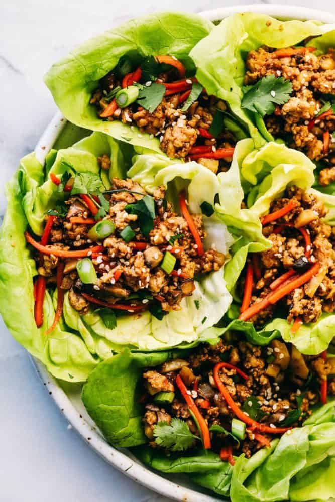 Asian turkey lettuce wrapsย are packed with intense flavorย from tender meat and seasoned, crunchy veggies. These light and tasty wraps are the perfect healthy appetizer or even dinner! Asian turkey lettuce wraps on a white plate.