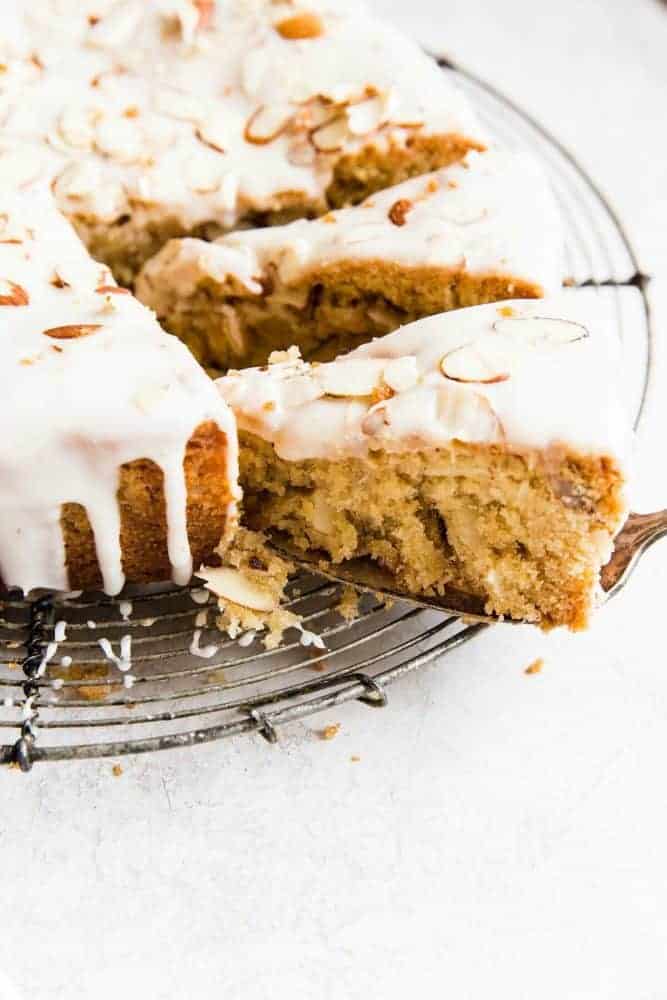 Easy Brown Butter Almond Cake is an incredibly delicious and moist cake with a brown butter icing. This is seriously one of the best cakes that I have EVER had! This is a must-make for that baking list! Brown butter almond cake on a cooling rack with a slice being removed.