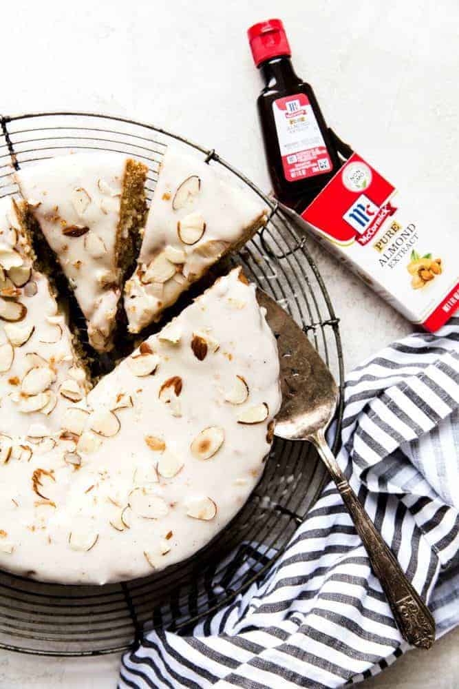 Easy Brown Butter Almond Cake is an incredibly delicious and moist cake with a brown butter icing. This is seriously one of the best cakes that I have EVER had! This is a must-make for that baking list! Brown butter Allman cake on a cooling rack with two slices about to be removed. There is also a small bottle of McCormick almond extract on the side.