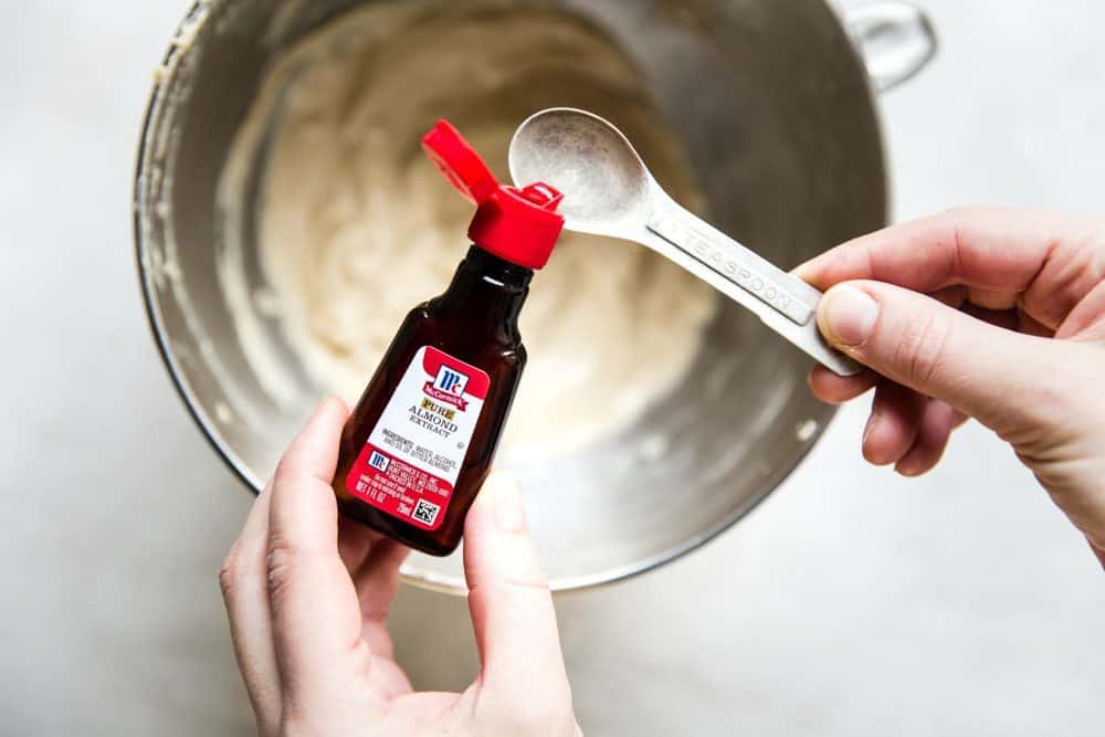 Easy Brown Butter Almond Cake is an incredibly delicious and moist cake with a brown butter icing. This is seriously one of the best cakes that I have EVER had! This is a must-make for that baking list! Hands measuring almond extract to be placed in with recipe.
