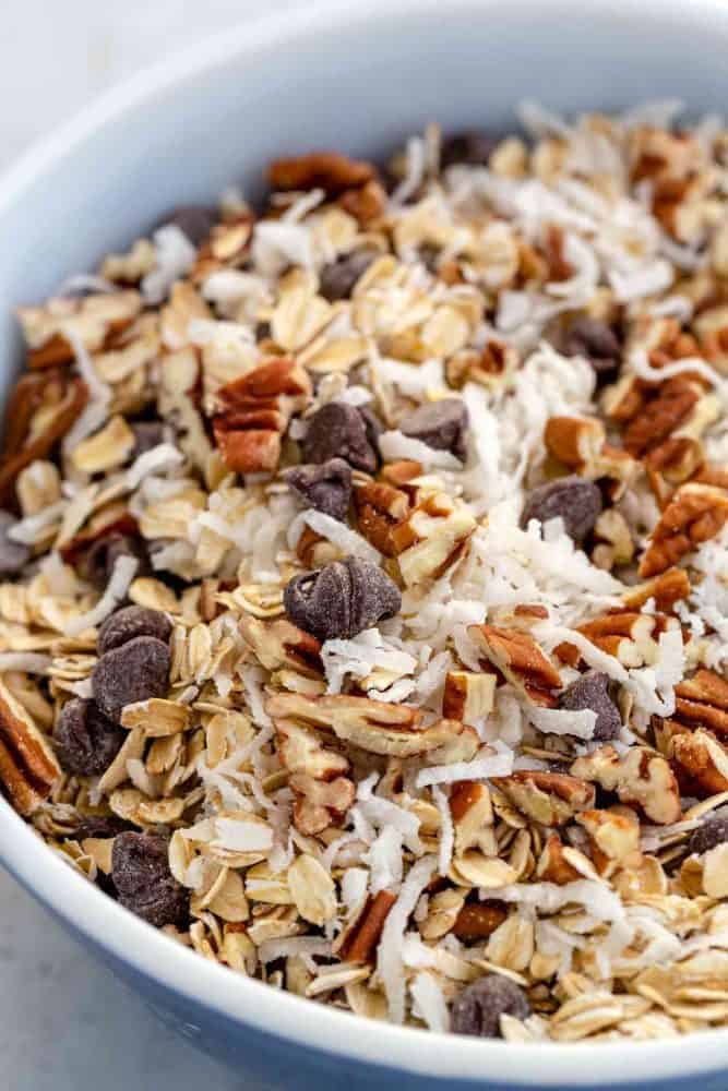 Cowboy Cookies are thick and chewy treats loaded with chocolate chips, oats, shredded coconut, pecans, and cinnamon. Incorporating browned butter into the cookie dough enhances the nutty, caramel notes of the cookie. This recipe packs delightful flavors and textures sure to satisfy any sweet tooth. Dried ingredients and chocolate chips in a mixing bowl.