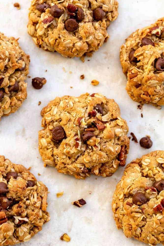 Cowboy Cookies are thick and chewy treats loaded with chocolate chips, oats, shredded coconut, pecans, and cinnamon. Incorporating browned butter into the cookie dough enhances the nutty, caramel notes of the cookie. This recipe packs delightful flavors and textures sure to satisfy any sweet tooth. Baked cowboy cookies on a parchment paper lined sheet pan.