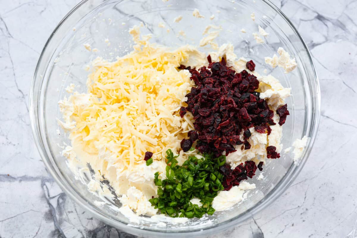 This festive cranberry pecan cheese ball is an easy appetizer for the holiday season! Everyone will love this creamy cheese ball loaded with delicious texture from the dried cranberries and pecans. Serve this impressive appetizer with crackers and enjoy! Second photo of the shredded cheese, cranberries and green onions added to the bowl.