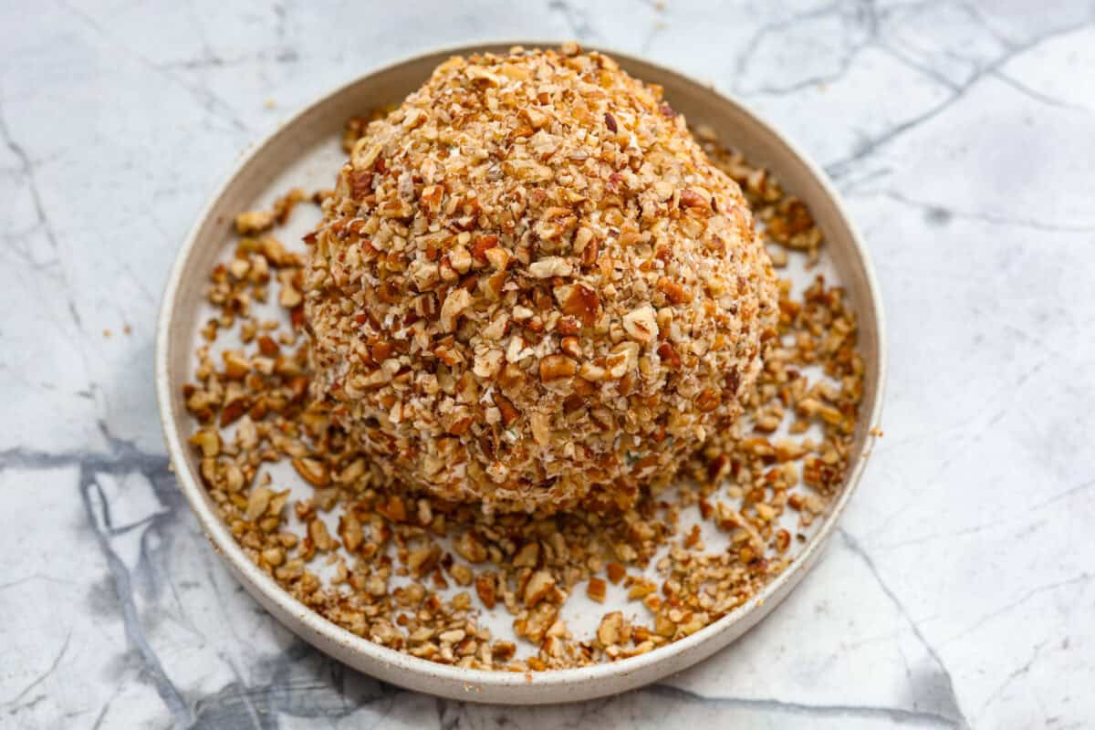 This festive cranberry pecan cheese ball is an easy appetizer for the holiday season! Everyone will love this creamy cheese ball loaded with delicious texture from the dried cranberries and pecans. Serve this impressive appetizer with crackers and enjoy! Fifth photo of the cheeseball rolling into pecans.