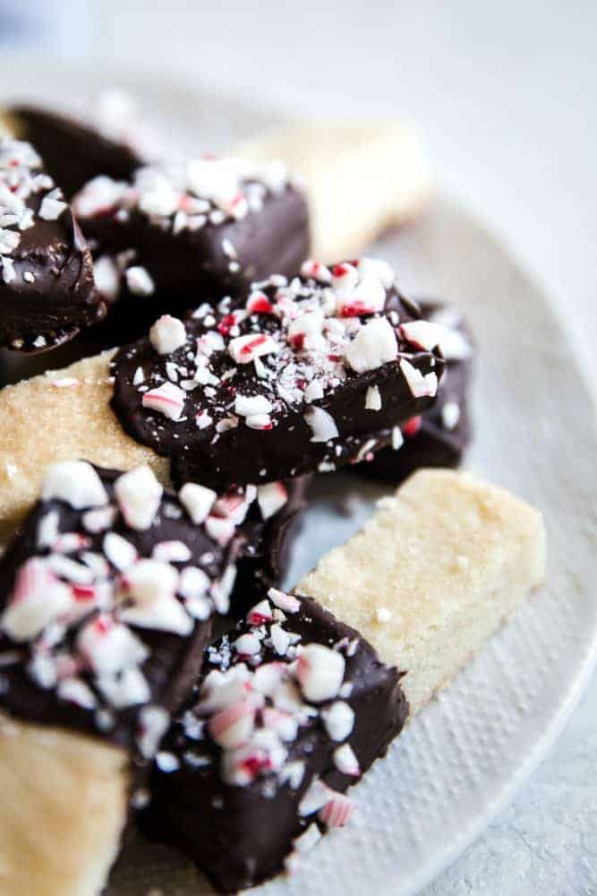 Chocolate Peppermint Dipped Shortbread Cookies are buttery, melt in your mouth shortbread cookies that get dipped in chocolate and sprinkled with crushed peppermint. These cookies make the perfect holiday treat! Close up photo of chocolate peppermint dip shortbread cookies on a white plate.