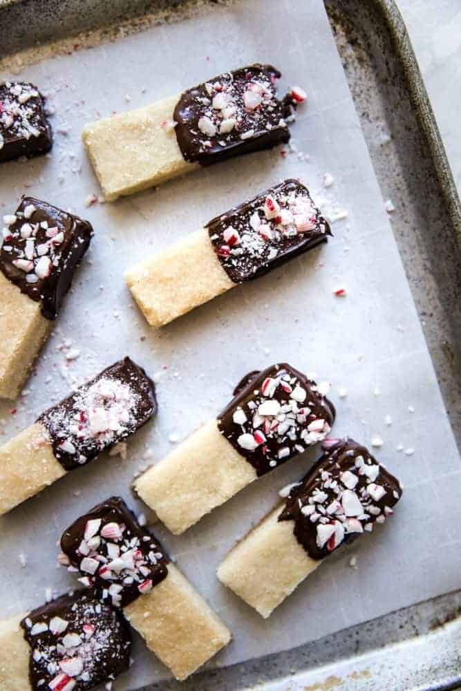Chocolate Peppermint Dipped Shortbread Cookies are buttery, melt in your mouth shortbread cookies that get dipped in chocolate and sprinkled with crushed peppermint. These cookies make the perfect holiday treat! Chocolate peppermint dipped shortbread cookies on parchment paper on a cooking sheet.