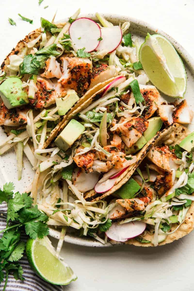 Smoky Paprika Fish Tacos with an Apple Slawย is one-of-a-kind Tacoย Tuesday kind of party with a flavorful, fun taste. You will not find a recipe with so manyย ingredients bursting with flavor and seasoning that puts smiles on everyones faces bite after bite. Thick, plump seasoned Smoky Paprika Fish that is lightย and tasty in every taco with a sweet crunch of Apple Slaw to make the perfect combination!ย Smoky Paprika Fish Tacos with an Apple Slaw on a white plate.