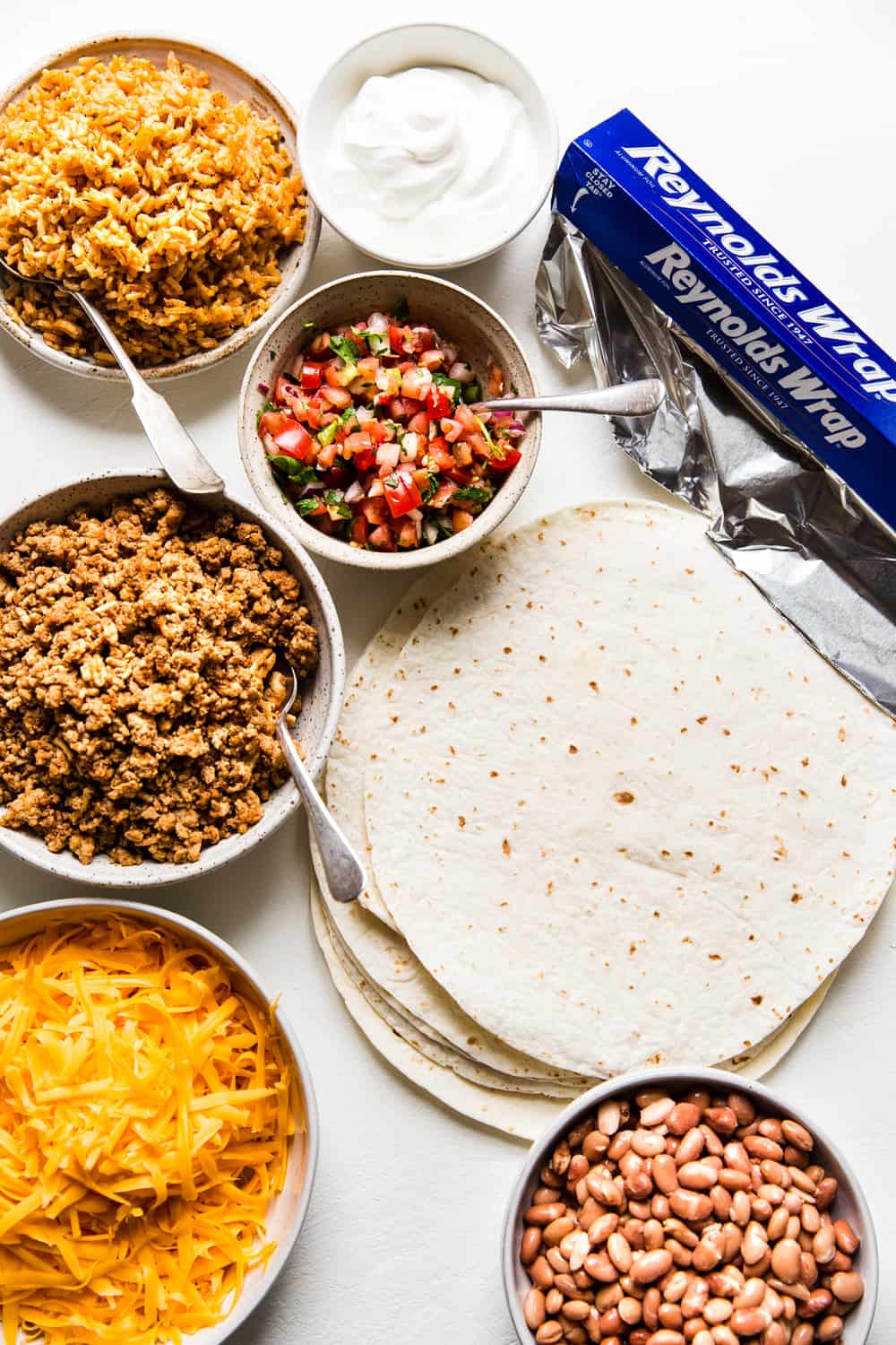 Easyย Mini Burritosย are packed with groundย chicken, pinto beans, Pico deย Gallo and flavorfulย Mexican rice. A classic burrito that is ready to show your tastebuds the next level. These Mini Burritos will leave you wanting more! All the ingredients for a burrito. Meat, cheese, tortillas, salsa, rice, beans, aluminum foil.
