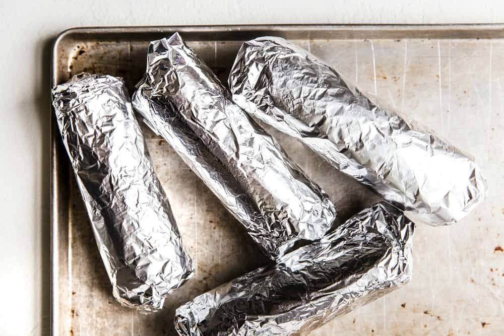 Easyย Mini Burritosย are packed with groundย chicken, pinto beans, Pico deย Gallo and flavorfulย Mexican rice. A classic burrito that is ready to show your tastebuds the next level. These Mini Burritos will leave you wanting more! 4 Burritos wrapped in aluminum foil on a baking sheet.
