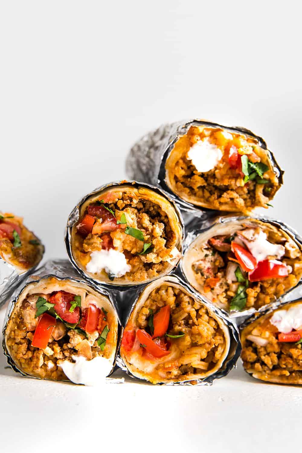 Easyย Mini Burritosย are packed with groundย chicken, pinto beans, Pico deย Gallo and flavorfulย Mexican rice. A classic burrito that is ready to show your tastebuds the next level. These Mini Burritos will leave you wanting more! A pyramid of burritos rolled up in aluminum foil.