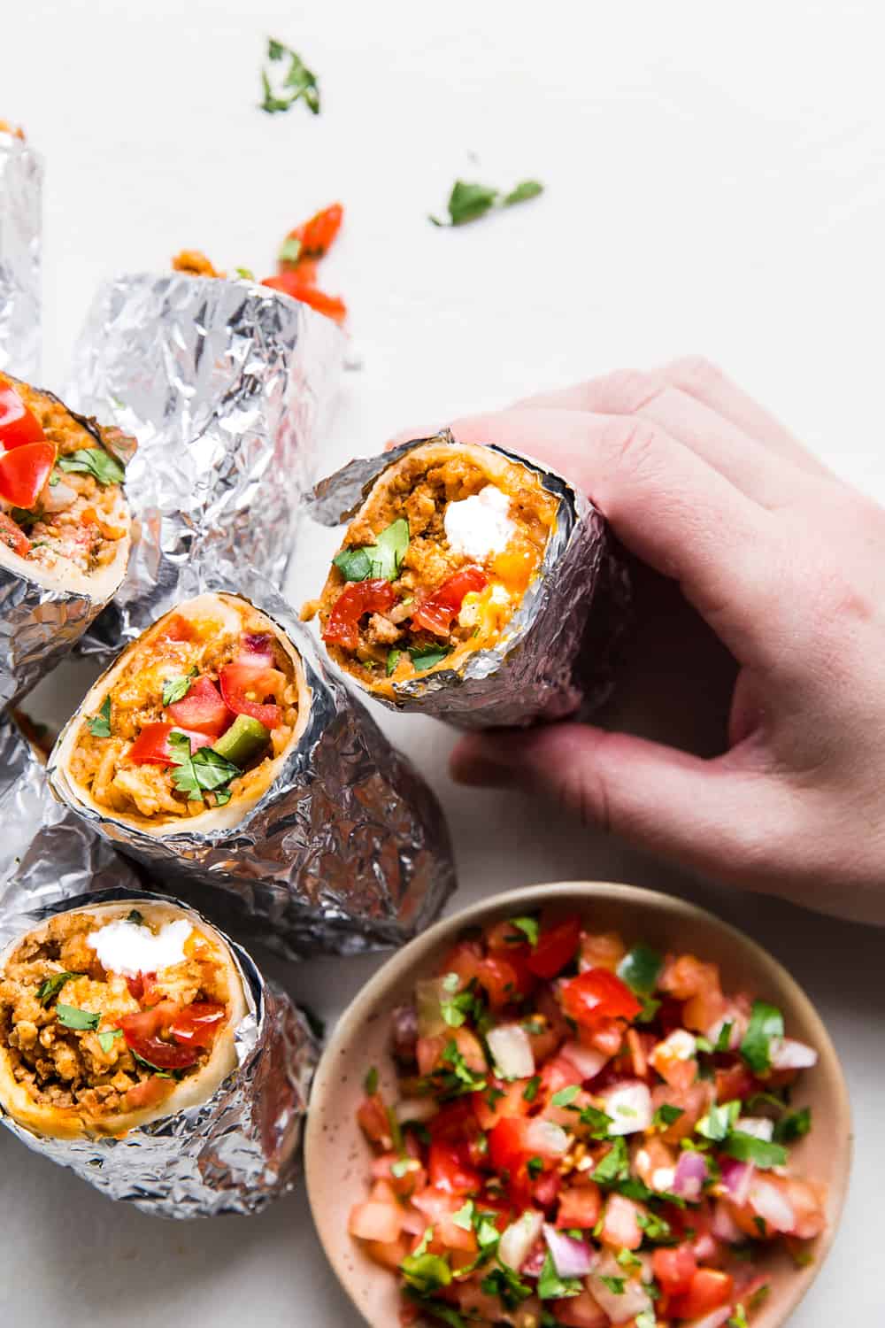 Easyย Mini Burritosย are packed with groundย chicken, pinto beans, Pico deย Gallo and flavorfulย Mexican rice. A classic burrito that is ready to show your tastebuds the next level. These Mini Burritos will leave you wanting more! Stack of mini burritos with a brown bowl of salsa on the side.
