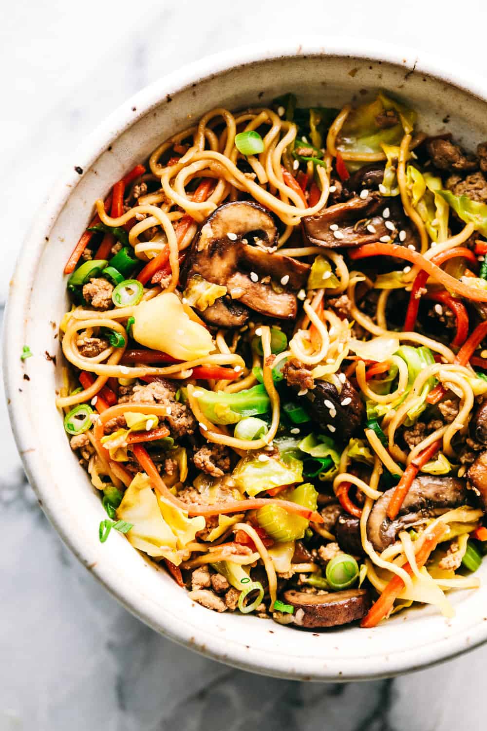 Egg Roll Noodle Skillet with Ground Porkย is filled withย tender bitesย of ground pork, soft cabbage, crunchy carrots and celery mixedย together with ramen noodles to make this mealย light and filling! The vegetables and noodles are coated with a sweet and spicy sauce that is full of flavor. This is all blended together in one simple skillet meal! Egg roll noodles with ground pork in a white dish.