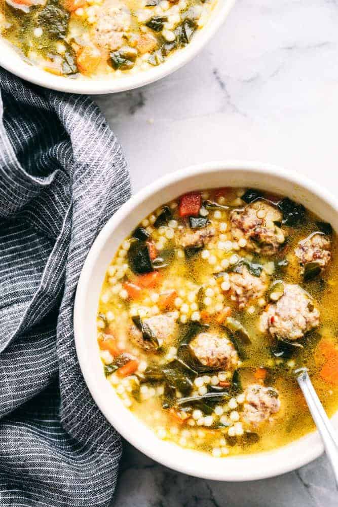 Italian wedding soup is warm and comforting and filled with tender chicken meatballs, veggies, and acini de Pepe. This classic Italian soup will become an instant family favorite! Two white bowls full of Italian wedding soup.