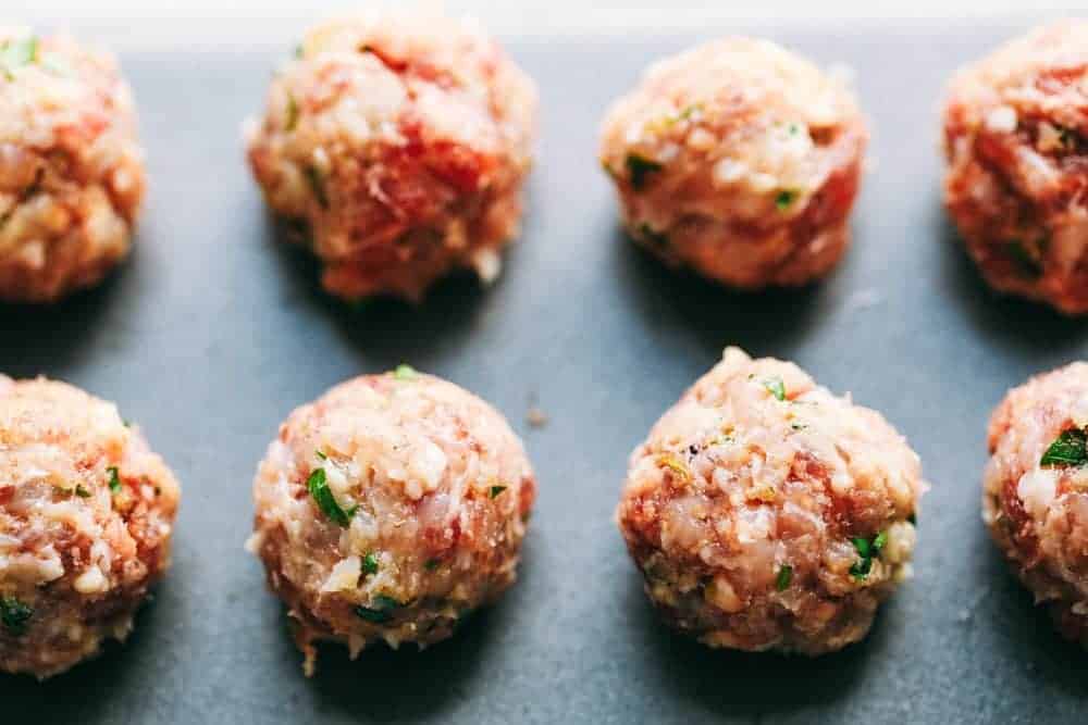 Italian wedding soup is warm and comforting and filled with tender chicken meatballs, veggies, and acini de Pepe. This classic Italian soup will become an instant family favorite! Raw meatballs on a sheet pan.