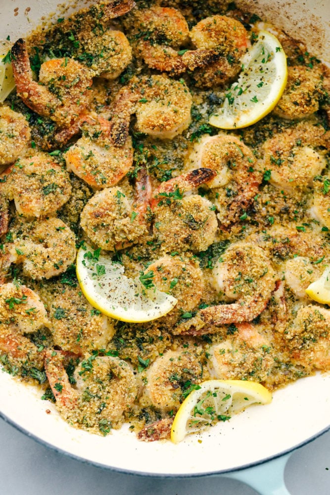 This Lemon Garlic Shrimp Scampi Recipe is a delicious 30 minute meal that cooks in a buttery, lemon garlic sauce and is breaded with a parmesan bread crumb topping. Combined, this meal is irresistible! A true restaurant quality meal right at home! Lemon garlic shrimp in a skillet with lemon wedges.