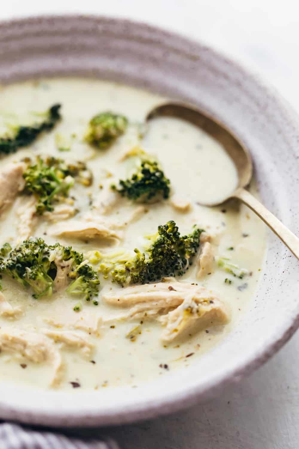 Creamy Chicken Broccoli Soup is a hearty soup that's perfect when you want something warm and comforting. Bite sized pieces of broccoli and shredded chicken are simmered in a broth flavoured with onions, celery and dried herbs. It's thick and creamy, and only takes 30 minutes to make. Closeup of creamy chicken broccoli soup in a bowl with a spoon