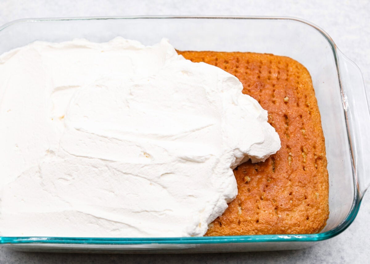 This tender Tres Leches cake is drenched in a three-milk mixture and is topped with fluffy whipped cream, cinnamon, or fresh fruit for a truly authentic Mexican dessert. Angle shot of the whipped cream topping being spread over the tres leches cake.