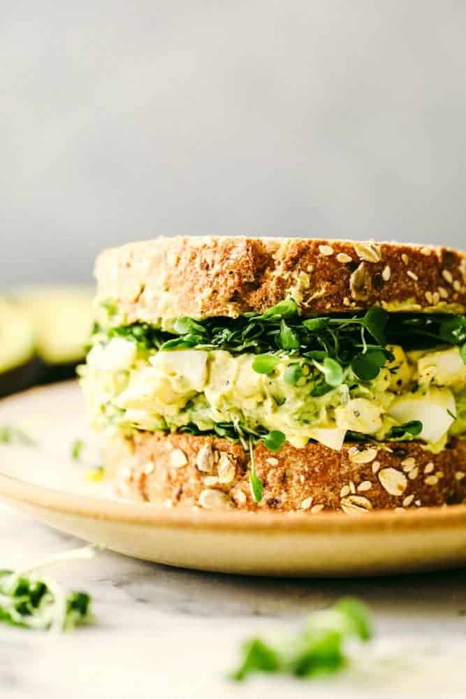 Avocado egg salad is a twist on egg salad adding in the avocado for the color and delicious flavor! Add this to any sandwich or eat it straight from the bowl, it will be a new favorite! Avocado egg salad on a sandwich on a plate.