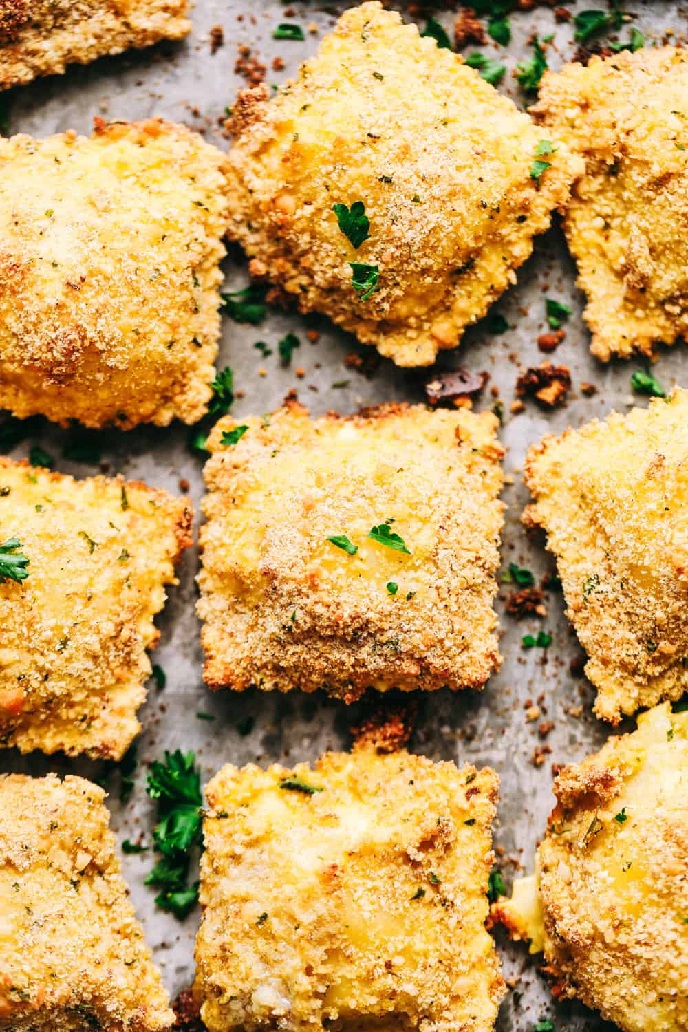 Crispy Baked Parmesan Ravioli are crunchy, crispy and filled with cheese and are perfect for dipping! These little bites are so addicting and good and will become a family favorite! Crispy Baked Parmesan Ravioli in rows on a baking sheet.