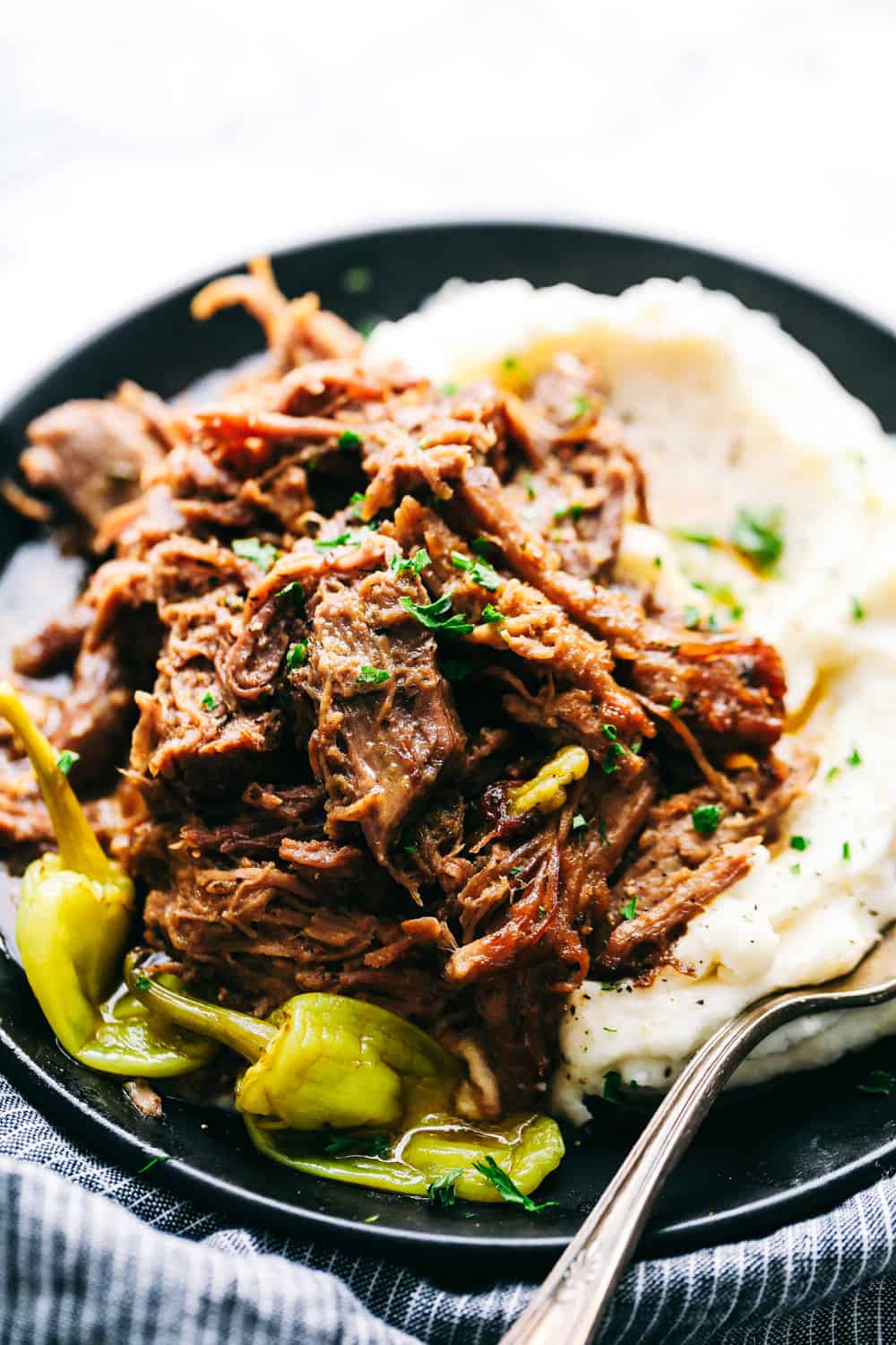 Slow Cooker Mississippi Pork Roastย is a savory, sweet and spicy pork roast that is tender to the touch and falls apart with ease. It takes minutes toย prepare and can be paired with a variety of sides. Your family will fall in love with this incredibly flavorful, melt in your mouth pork roast!ย Pork roast on a plate with mashed potatoes.