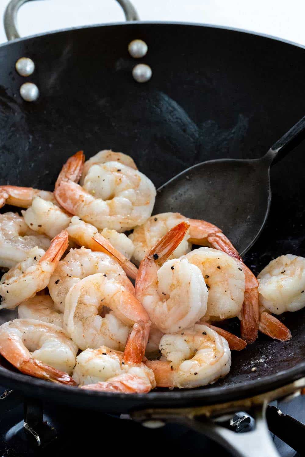 Sweet and Sour Shrimp is a quick Chinese meal made all in on pot! Succulent seafood is stir-fried with bell peppers, zucchini, pineapple and then tossed in a tangy honey sauce. This dish comes together in just 20 minutes for a simple and flavorful dinner. shrimp cooking in a wok