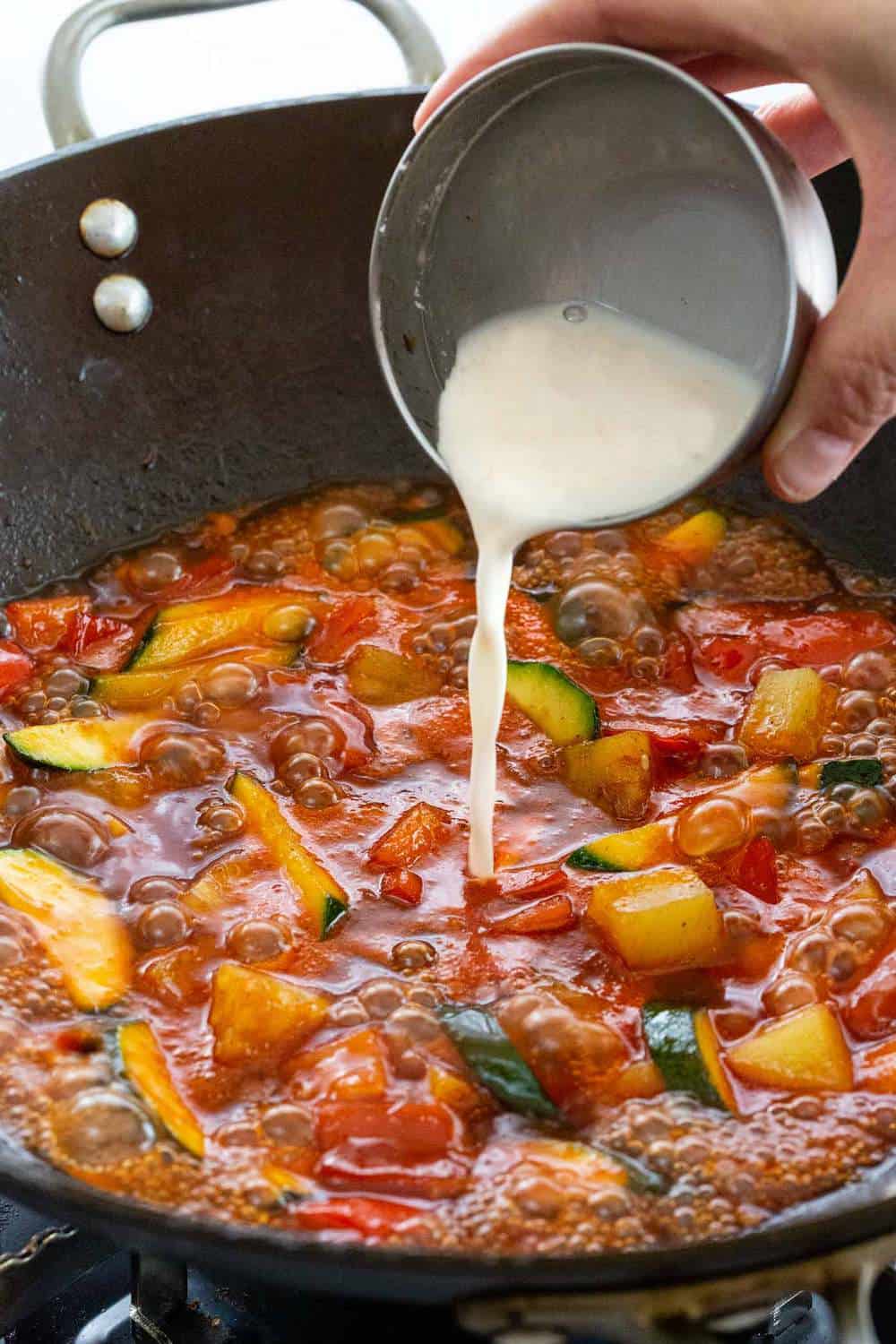 Sweet and Sour Shrimp is a quick Chinese meal made all in on pot! Succulent seafood is stir-fried with bell peppers, zucchini, pineapple and then tossed in a tangy honey sauce. This dish comes together in just 20 minutes for a simple and flavorful dinner. cornstarch being poured into a wok to make sauce